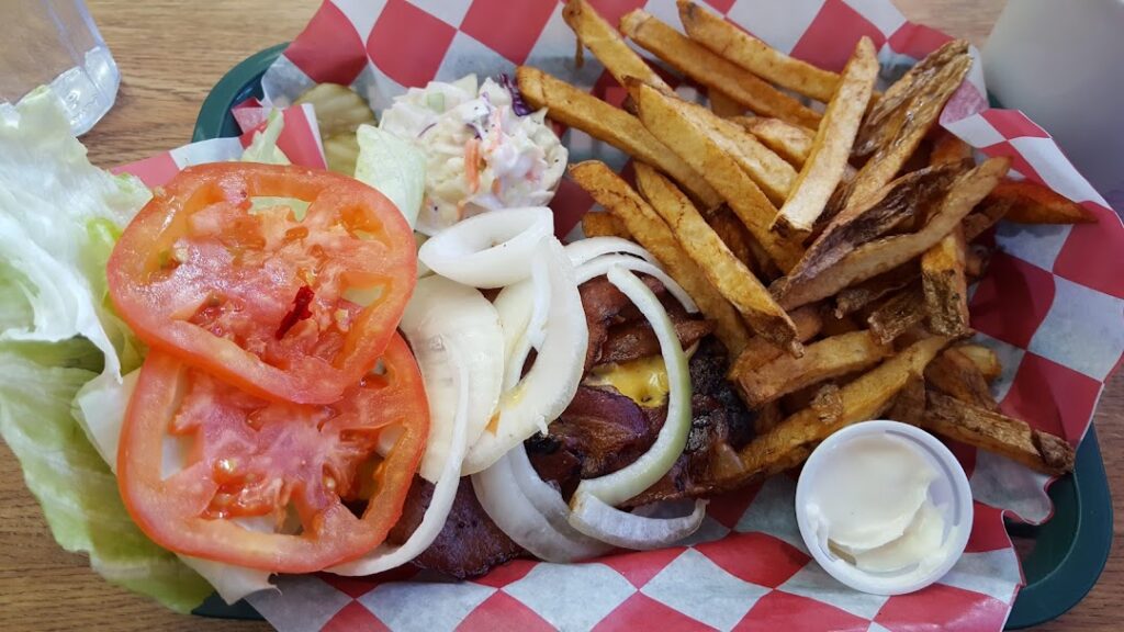 A plate of food that includes french fries, a burger, onions, tomatoes and coleslaw.