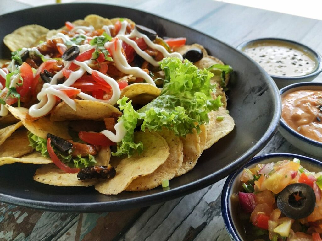 Dish of nachos covered in sour cream, tomatoes, olives and lettuce with dipping sauces.