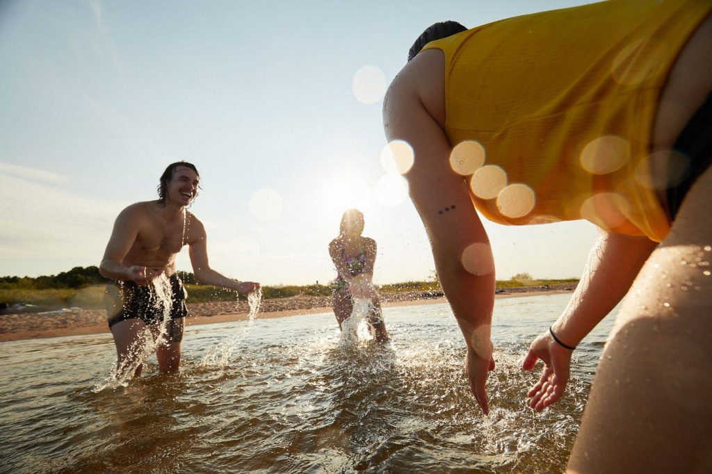 Three adults splashing each other in Lake Superior. The sun is shining on them.