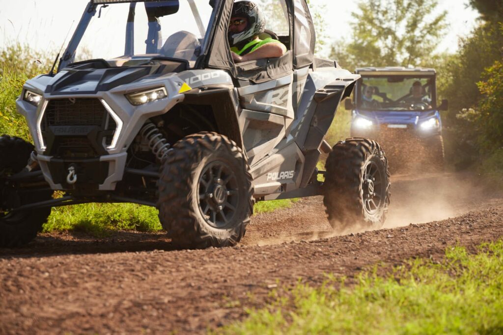 Two ATVs kicking up mud on a trail.