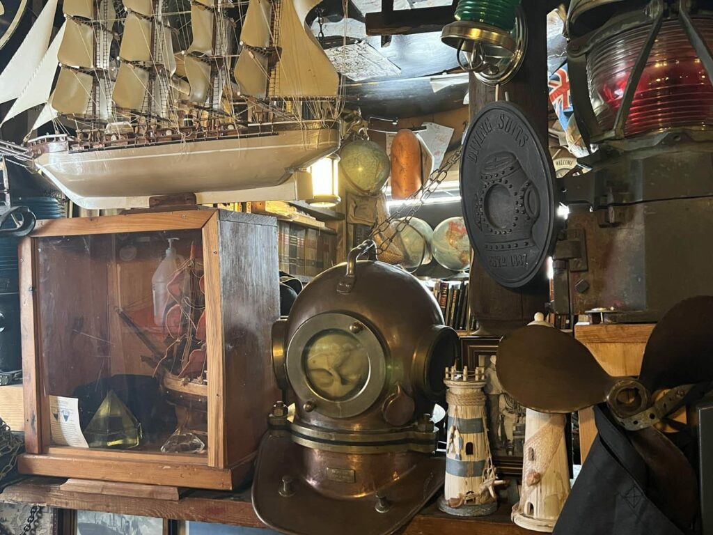 Decorations in the Anchor bar which include a five mast model sailboat, railroad lanterns, an old propeller, small, wooden lighthouses, a metal deep sea diving oxygen hood, and globes of the earth.