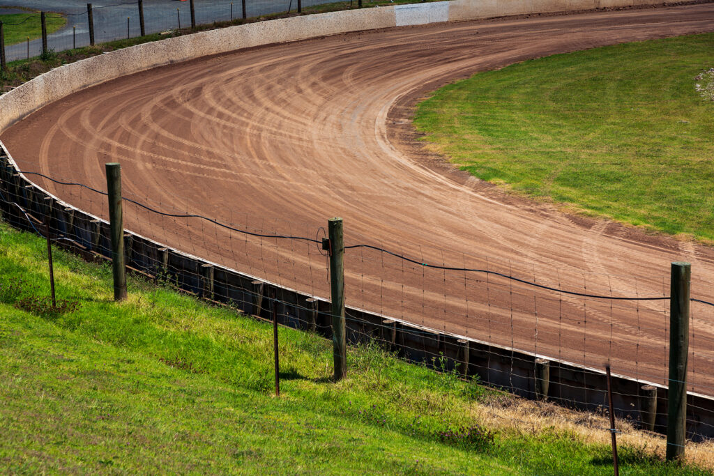 A an empty dirt speedway track with lots of tire tracks around a sharp corner