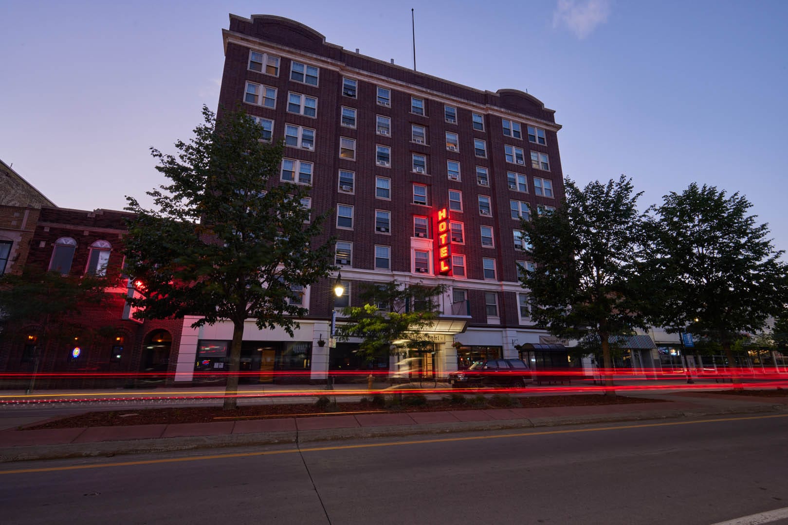 The exterior of the Androy Hotel at night with a car's lights blurred as they go past. A sign reads HOTEL in red neon letters.