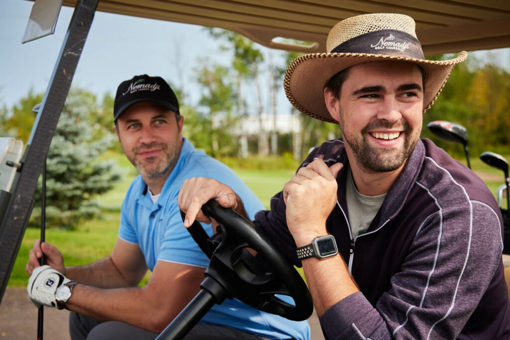 Two men in golf gear are smiling on a golf cart.