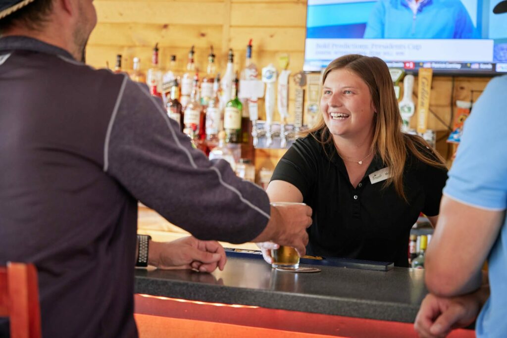 Smiling bartender serves a beer to her two customers.