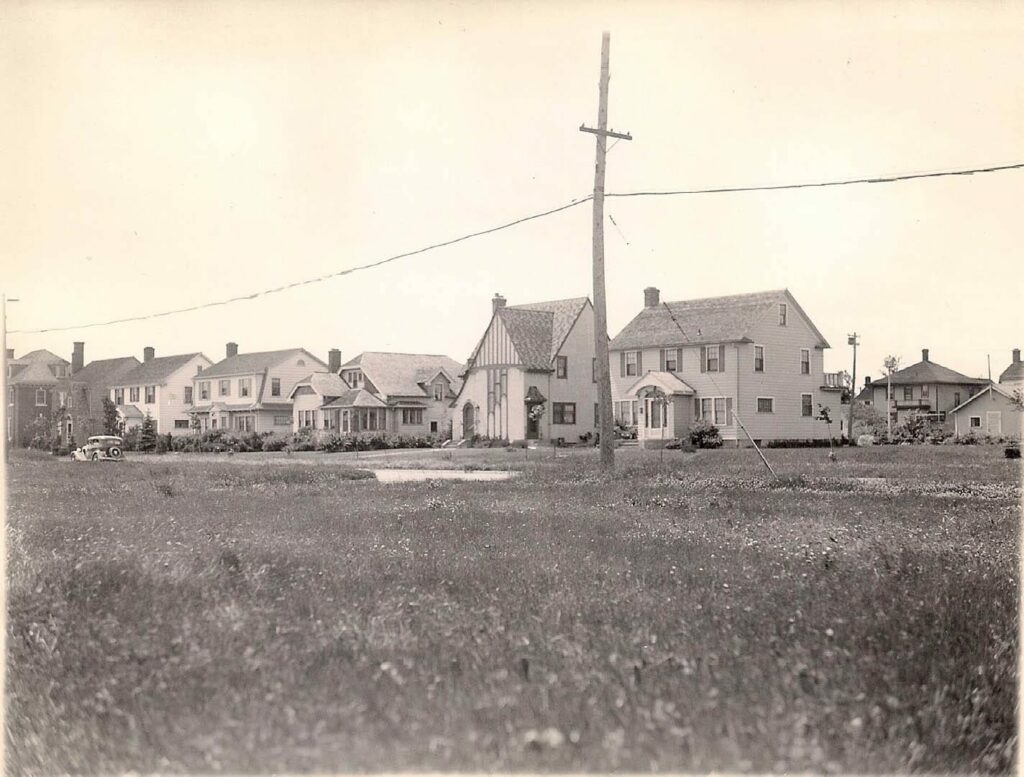 An old, sepia-toned photo of two story homes on Hammond Avenue. They're built very close to each other and there are no trees. In the foreground is an electrical pole.