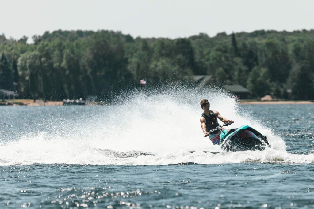 A young man on a jet ski is making a large wake and spray as he turns sharply in an inland lake in the summer.