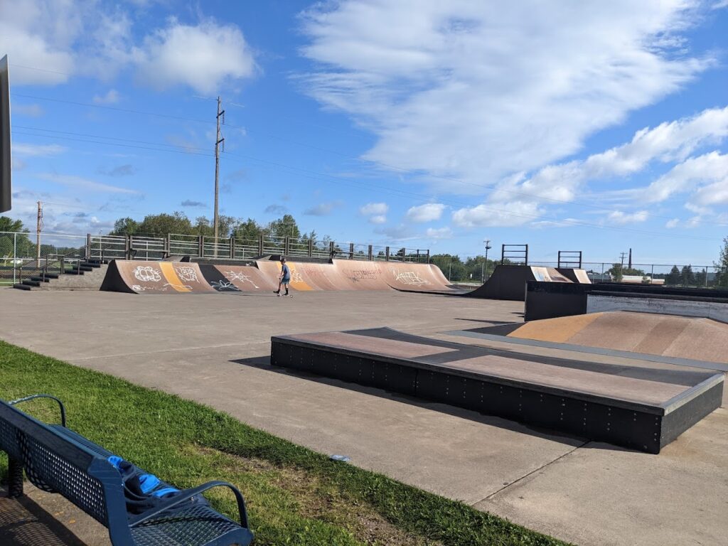 A single young teen in a skate park with a lot of ramps and drops to play on.