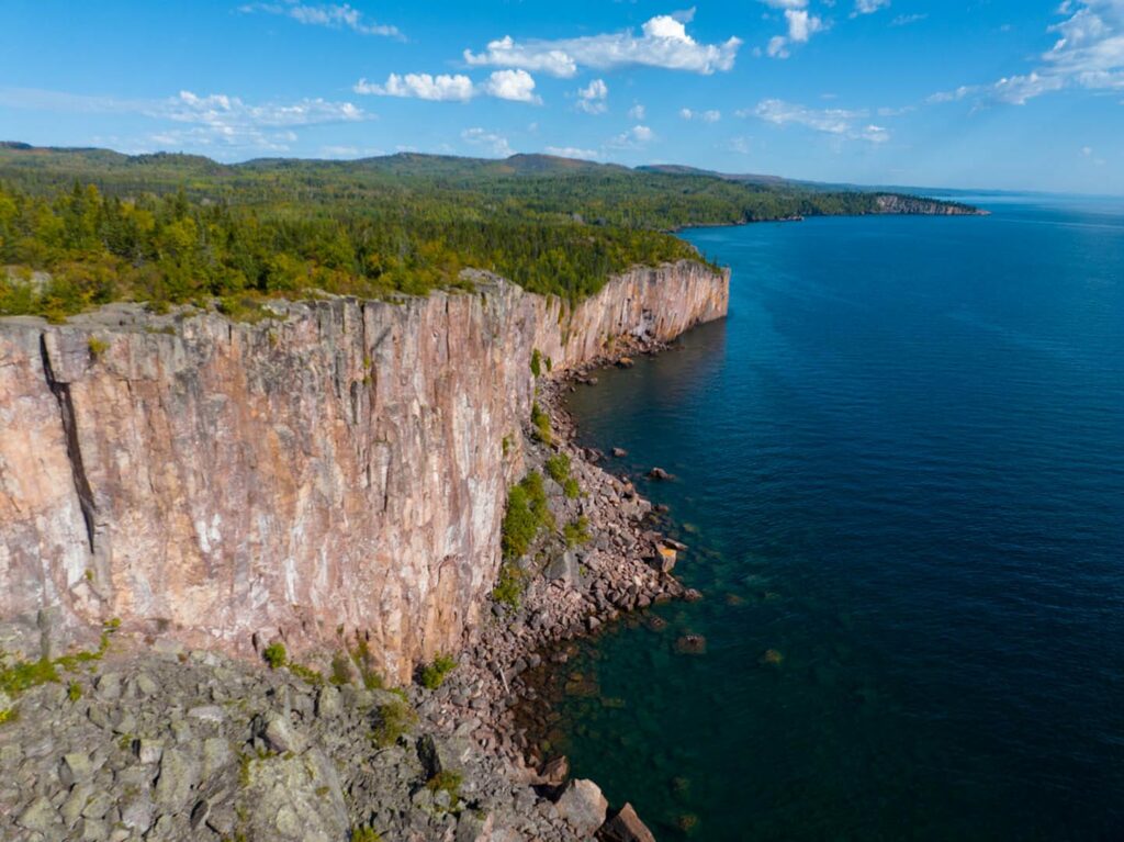 A birds-eye view of Palisade Head tall cliff with a rocky bottom and a full view of Lake Superior's rocky and jagged north shore.