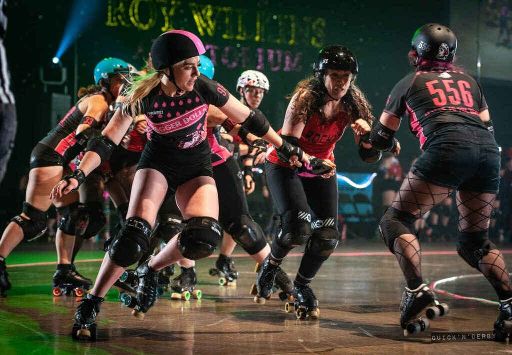 A group of women in roller derby gear skating on a roller track.
