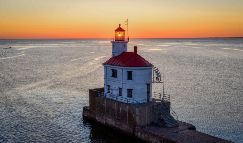 Lighthouse on Wisconsin point with the sun setting in the background. The lighthouse has a red roof and white base.