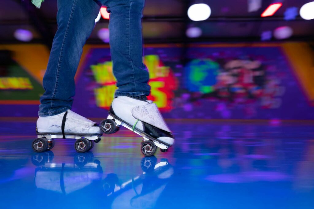 A closeup look at some white roller skates on a brightly colored, blue and purple dance floor.