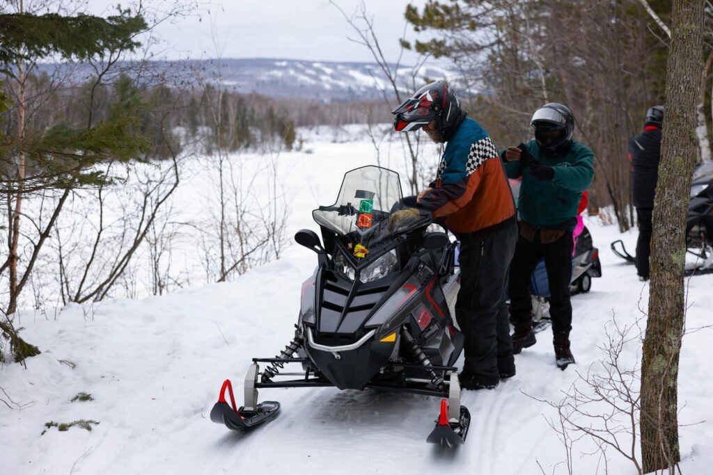 Three snowmobilers stop for a break over a vista of the St. Louis River on the Wisconsin side. Across the river, we can see Spirit Mountain's ski hills covered in snow.