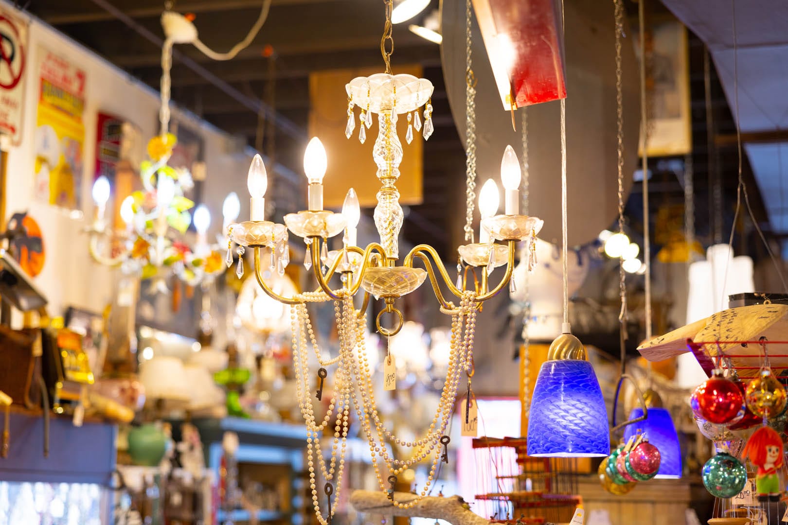 Antique lamps and lights and Christmas ornaments hang from the ceiling in an antique store.