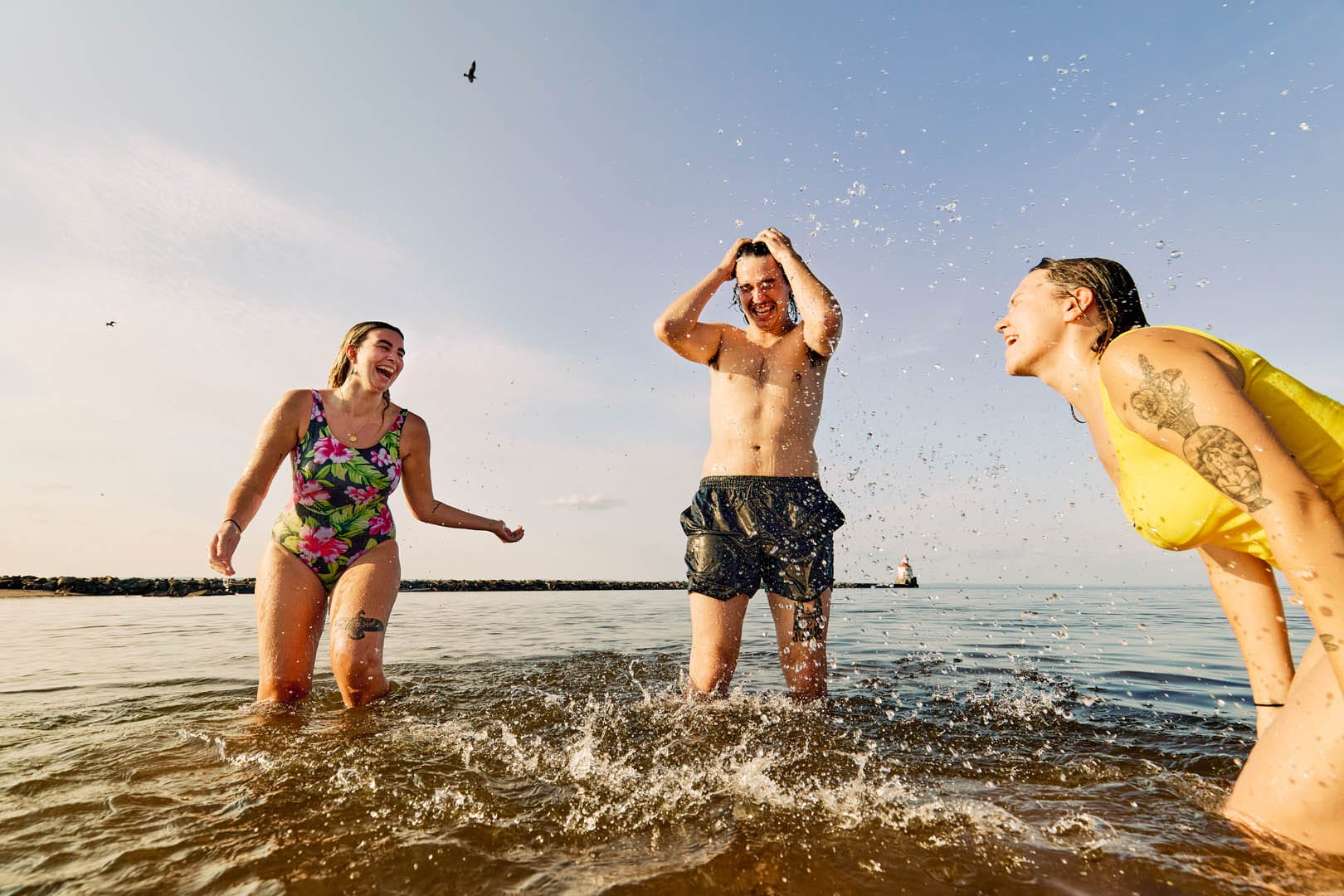 Three people having fun swimming in Lake Superior splashing each other and laughing. The sun is very warm but the water is most likely cold.