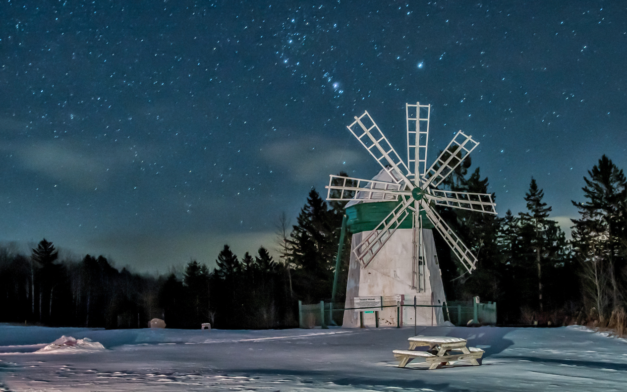 An old white and green windmill in the snow at night with a starry sky