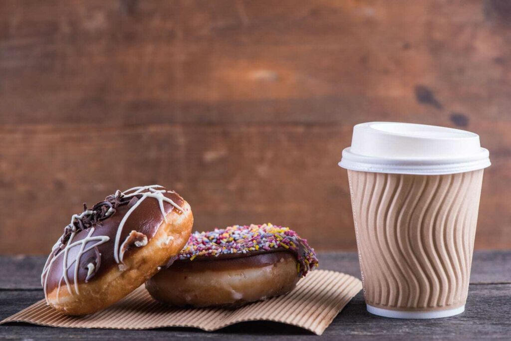 Two chocolate donuts sit beside a to-go cup of coffee.