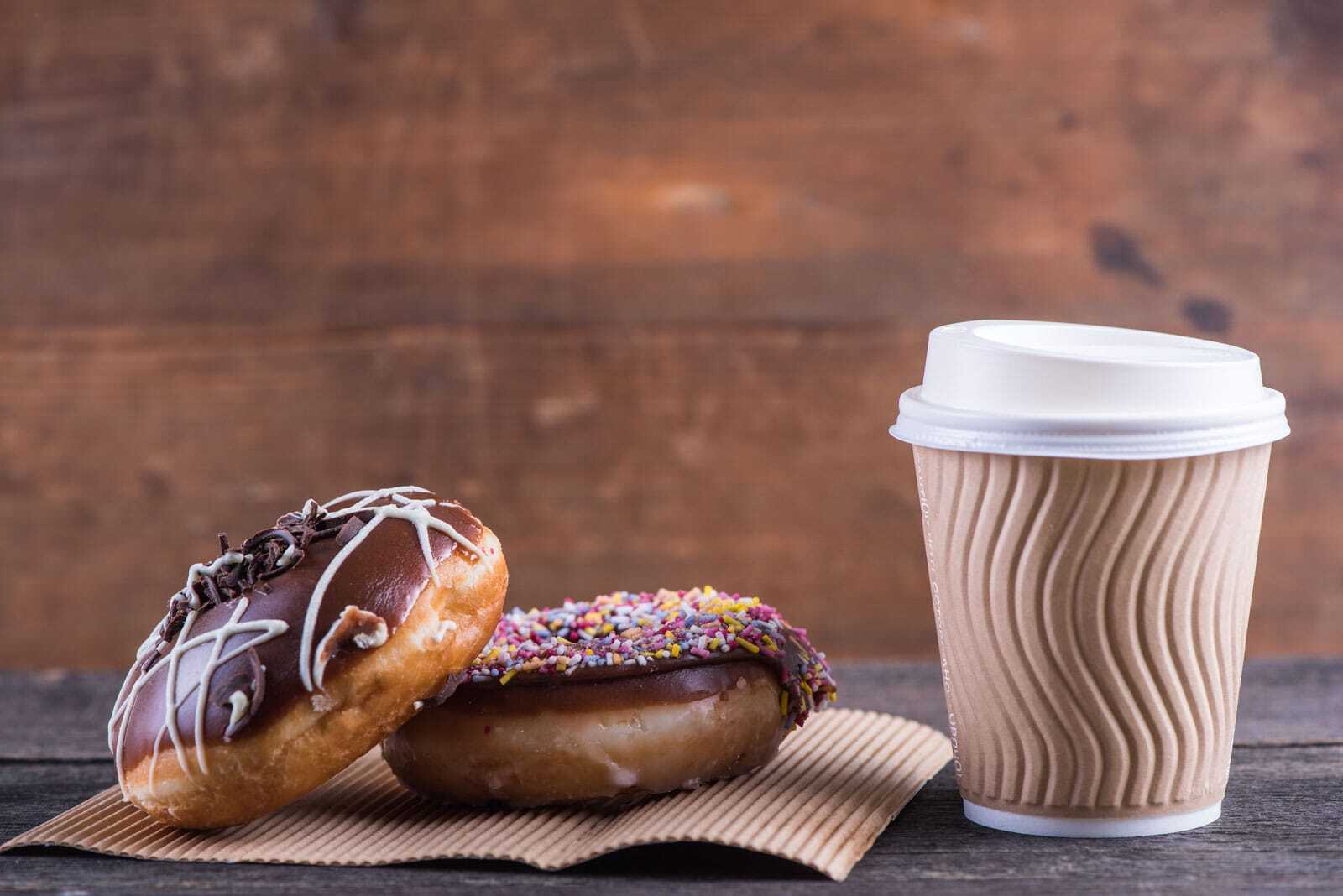 Two chocolate donuts sit beside a to-go cup of coffee.