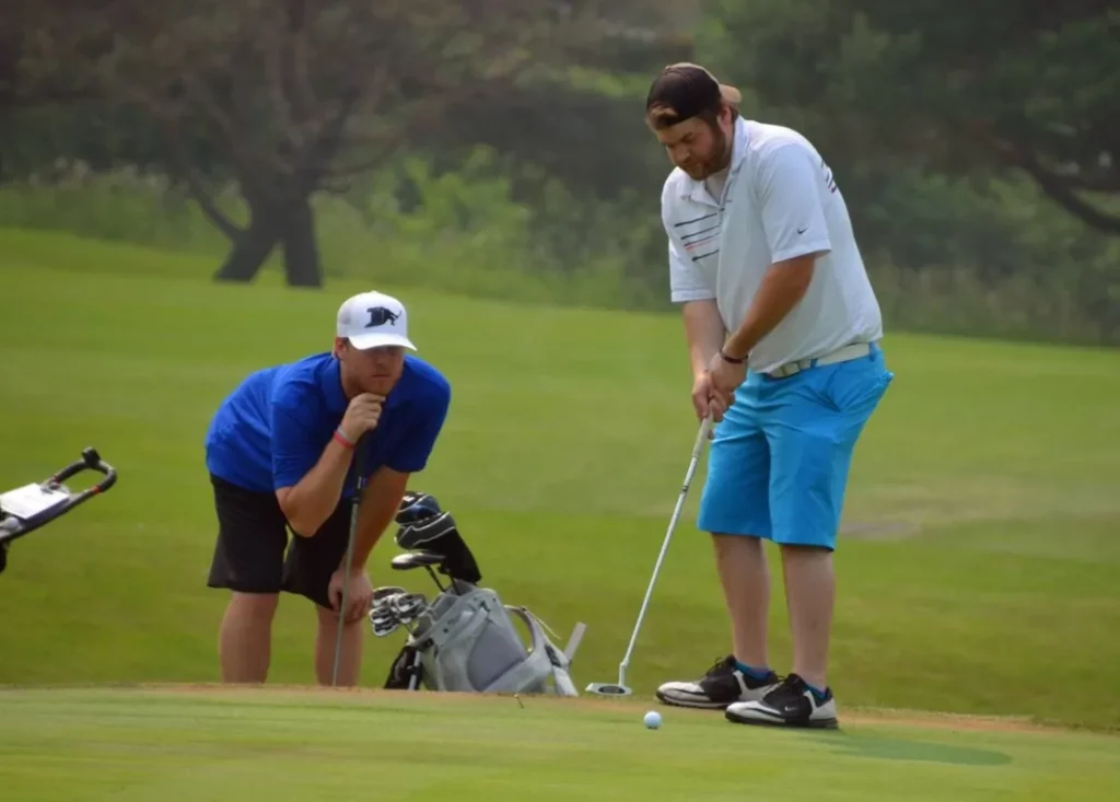 Two men at a golf course. One is lining up his shot while the other one observes.