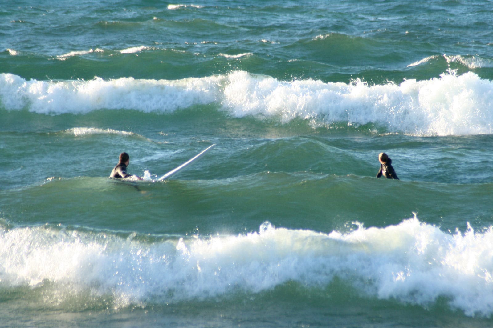 Two people floating in large waves on Lake Superior waiting for the perfect wave to catch and surf. There are large whitecaps and the waves are close to 8 feet tall.