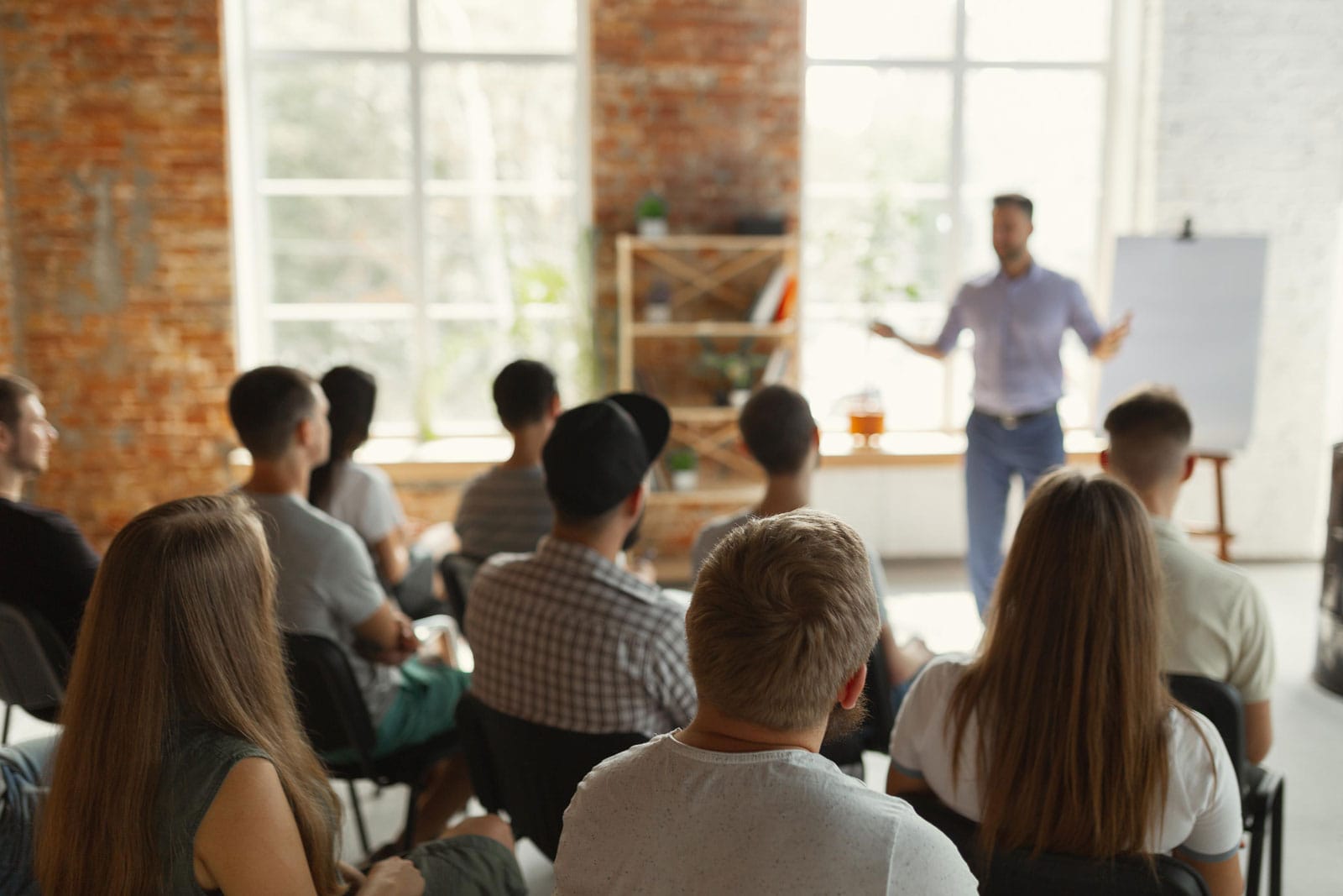 A crowd sitting at a presentation with a person directing toward a whiteboard.