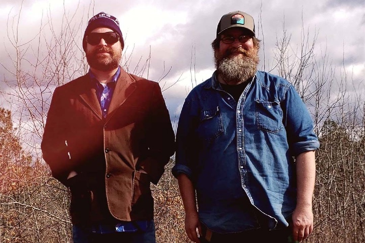 Two middle aged men standing in the woods.