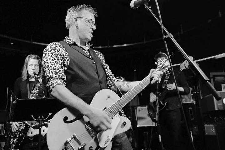 A black and white photo of a man playing the guitar in a band.