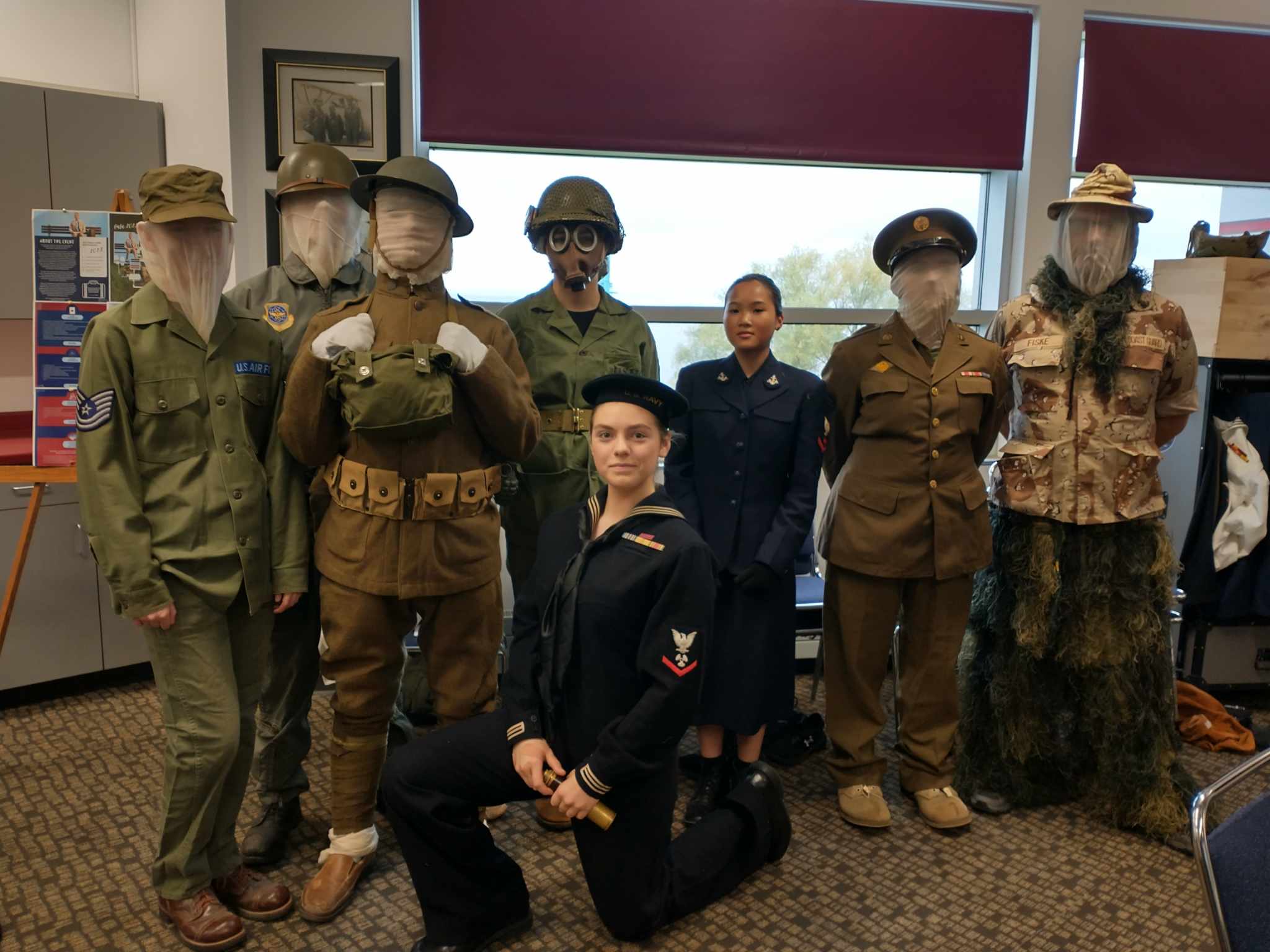 Eight individuals dressed up like statues of soldiers in an office.