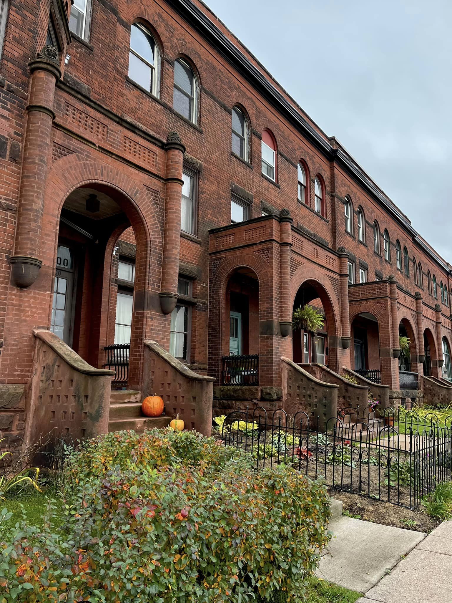 The exterior of an old building with red brick and steps leading up to the doors with bushes in front.