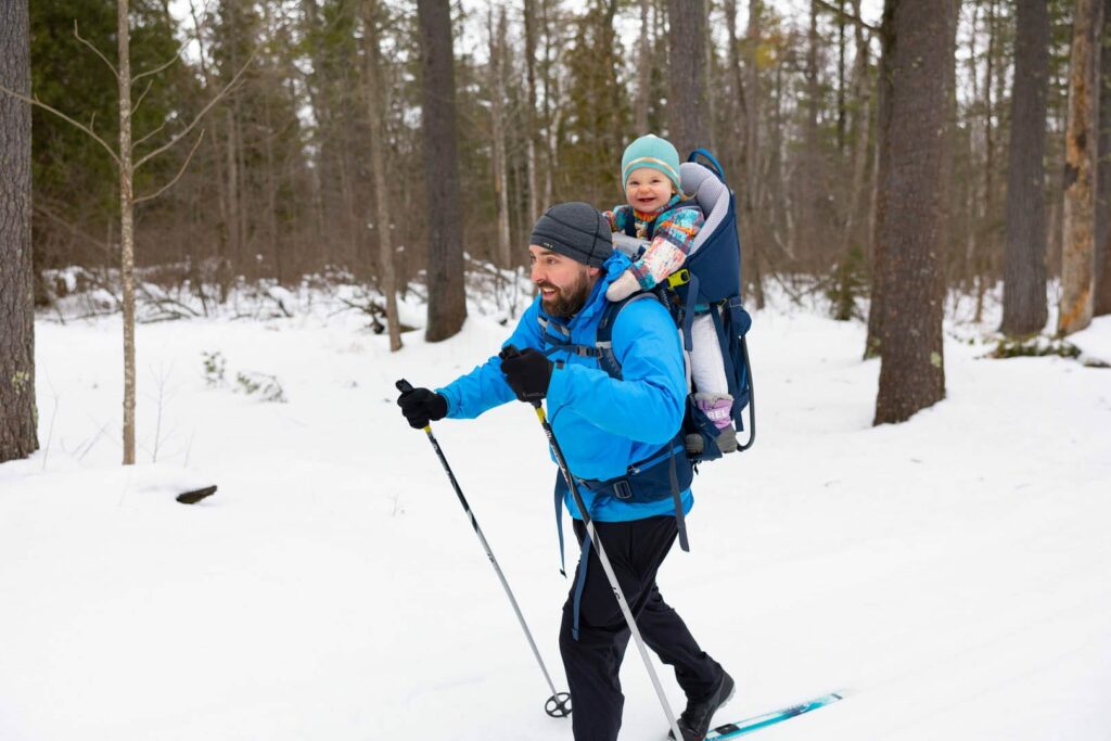 Parent cross country skiing and carrying toddler child on his back