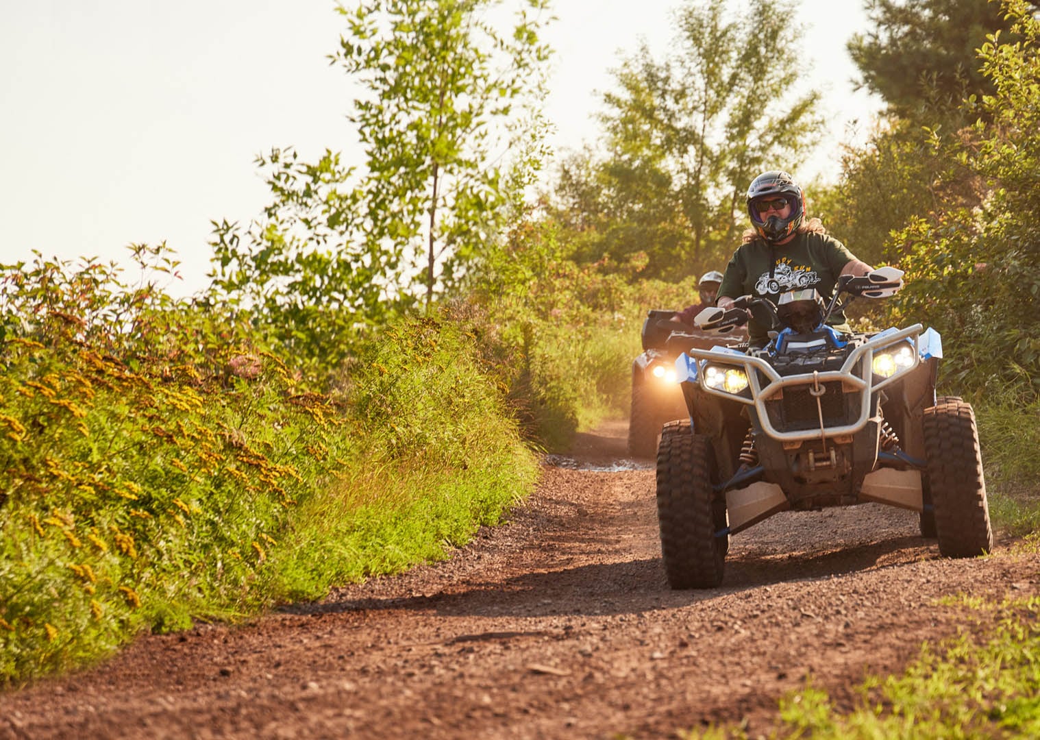 Two people each on their own ATV riding down a dirt trail.