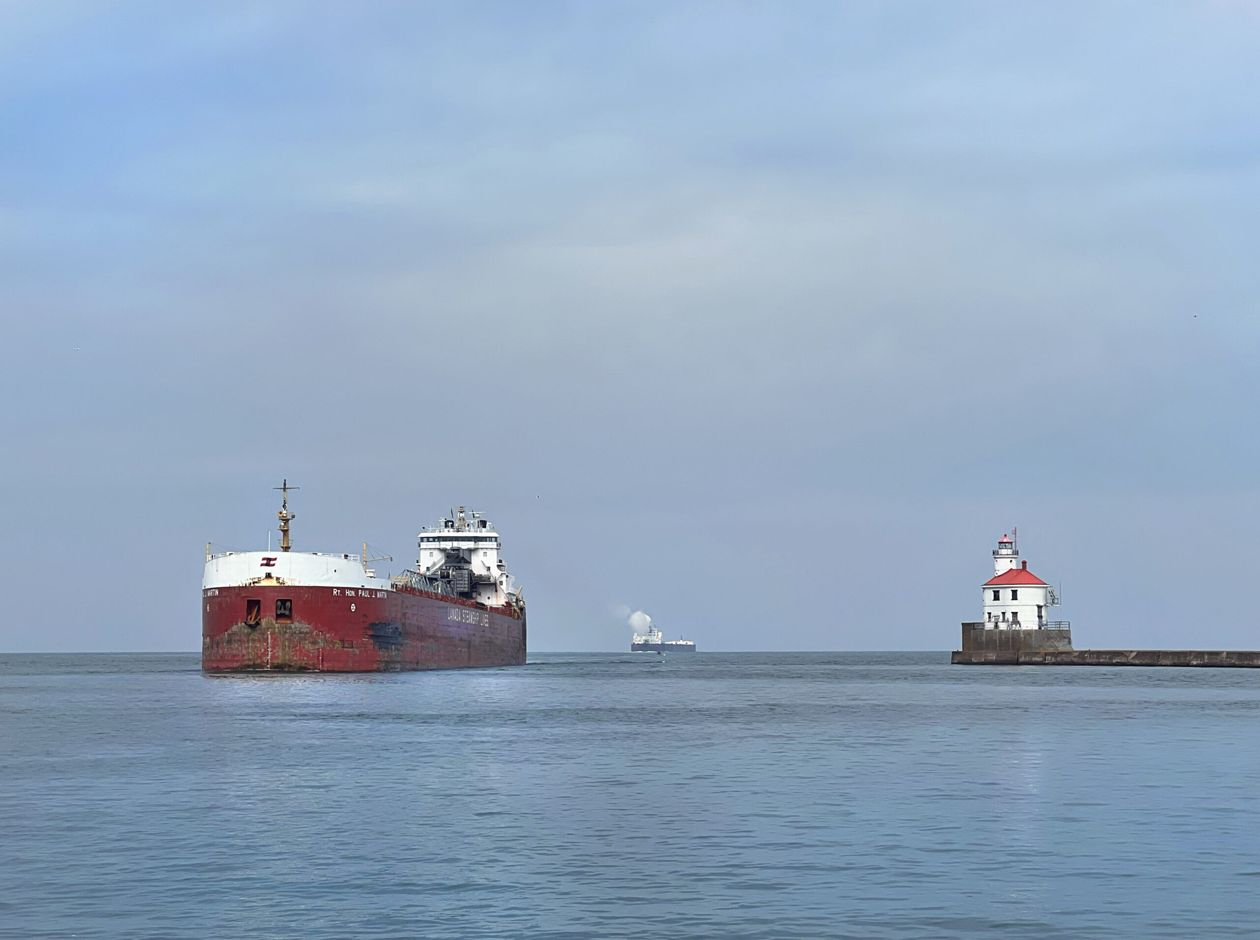 A large ship moving through the canal at Wisconsin Point with a lighthouse in the background.