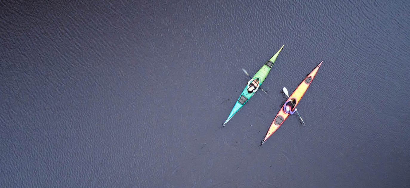 An overhead image of two kayakers paddling on calm water.