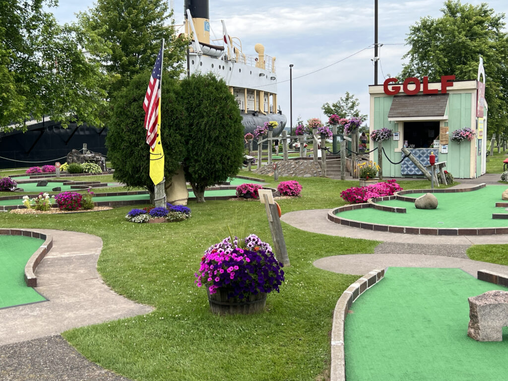 A brightly colored mini golf course with lots of pink and purple flowers in baskets.