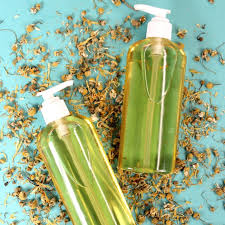 Two clear pump bottles filled with yellow liquid sit on a light blue surface scattered with dried flowers. The scene suggests a natural, botanical theme, perhaps related to skincare or haircare products.