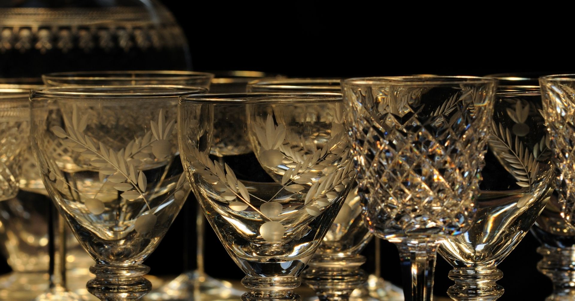 A collection of intricately engraved crystal glasses, featuring floral and geometric patterns, is displayed against a dark background, highlighting their detailed designs and reflective surfaces.