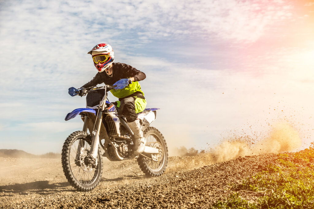 Young man in helment riding a dirt bike kicking back dirt.