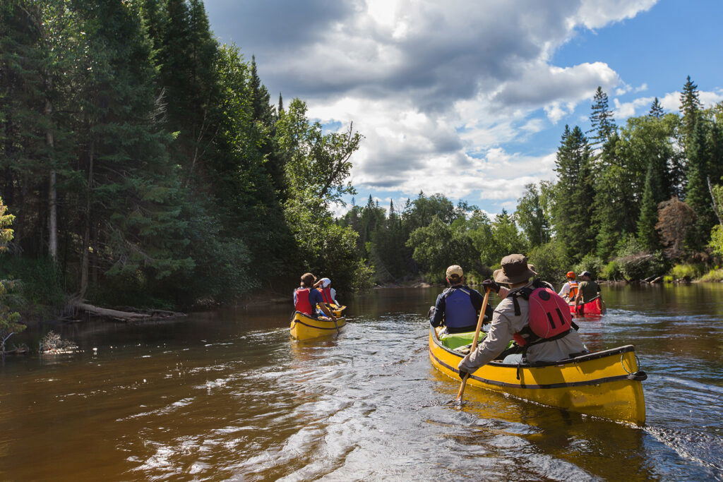 A group of people in canoes paddles down a river, enjoying one of the popular summer activities in Superior, Wisconsin.