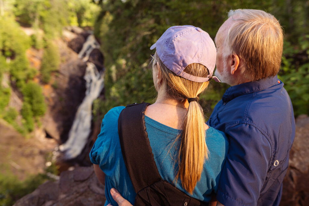 A man and woman stand on a rock admiring a waterfall, enjoying one of the best summer activities in Superior Wisconsin.