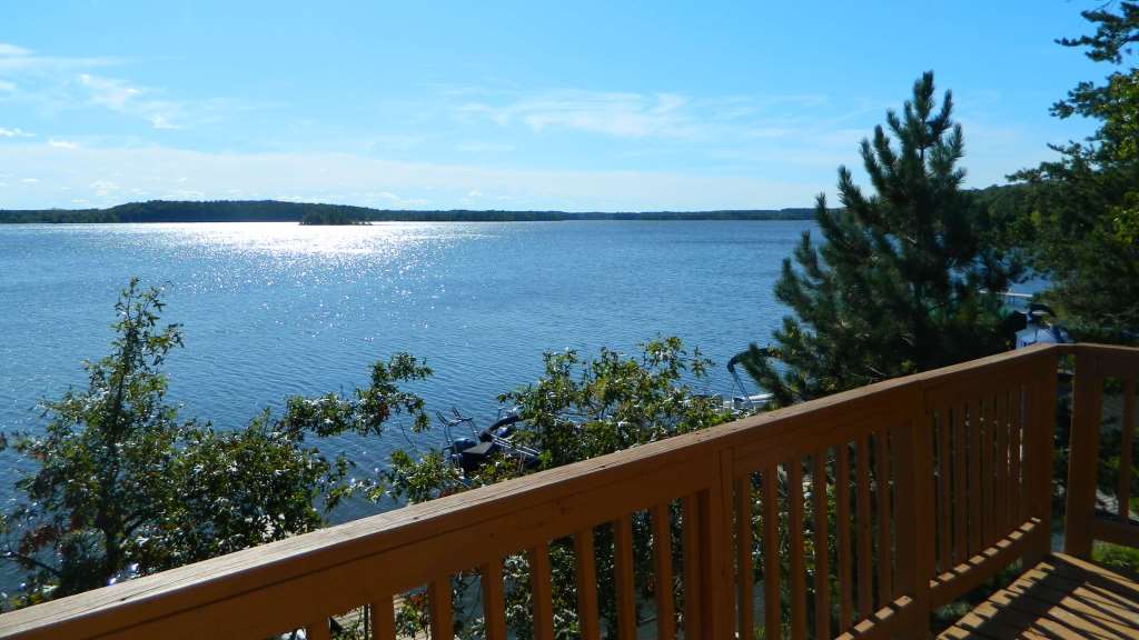 View of a lake with sunlight reflecting on the water, seen from a wooden deck surrounded by green trees under a clear blue sky—perfect for enjoying summer activities in Superior Wisconsin.