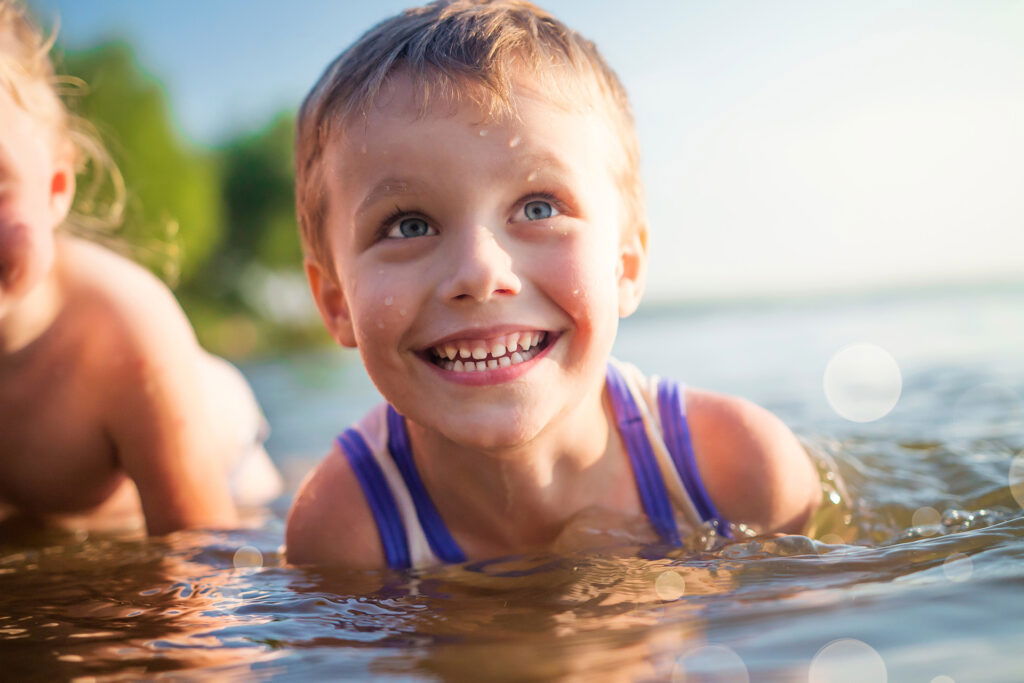 A very closeup photo of a young boy who is swimming with friends in a lake. He is smiling and looking at someone