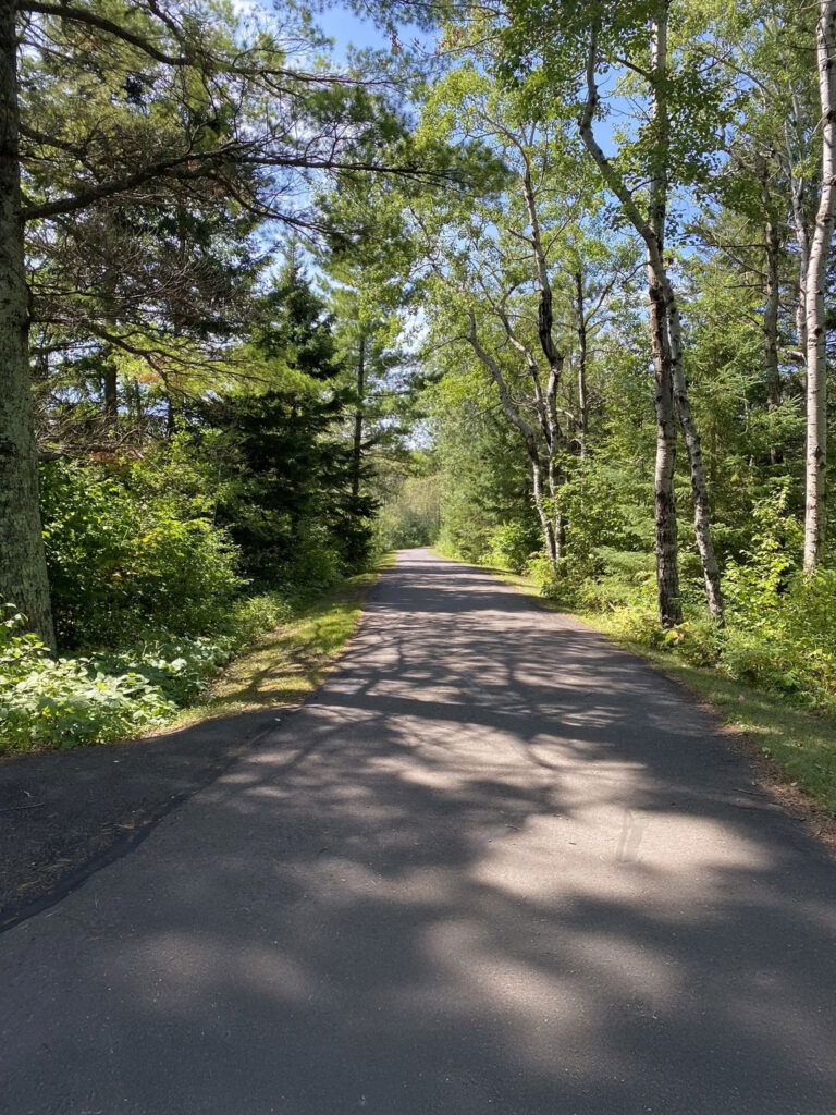 A sunset view over a calm ocean, with orange and yellow hues in the sky reflecting on the water, and gentle waves approaching the sandy shore in the foreground.
