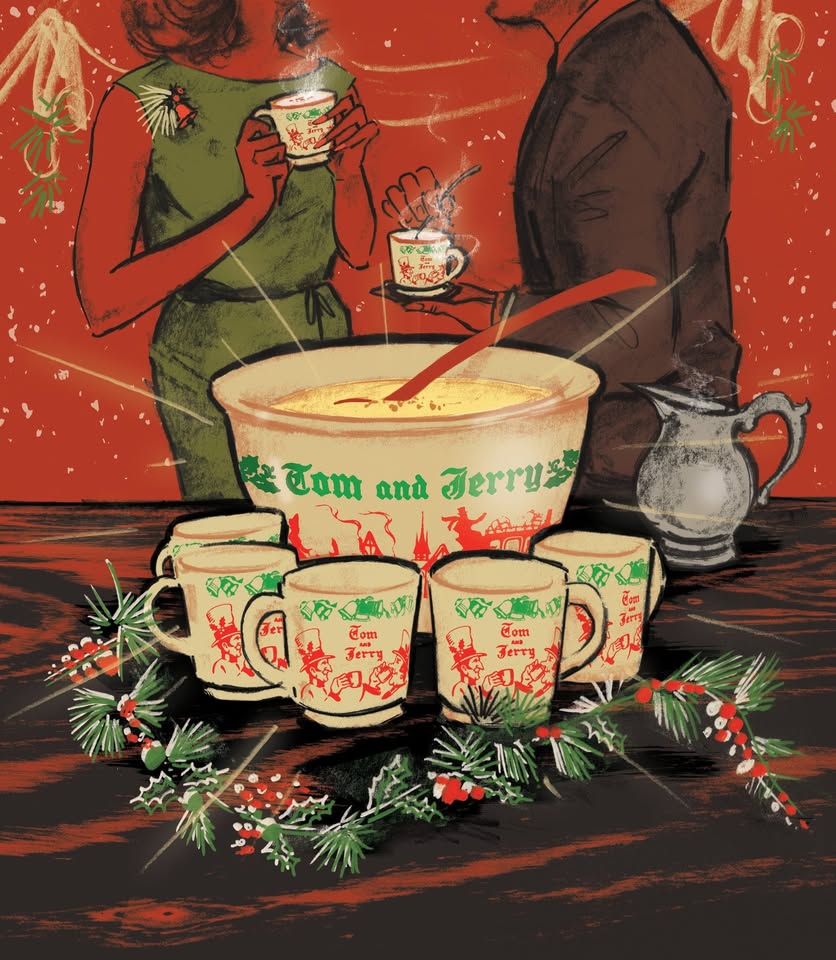 Two people hold steaming cups near a large festive bowl labeled "Tom and Jerry," surrounded by decorated cups, a silver pitcher, and pine holiday garland on a wooden table against a red background.