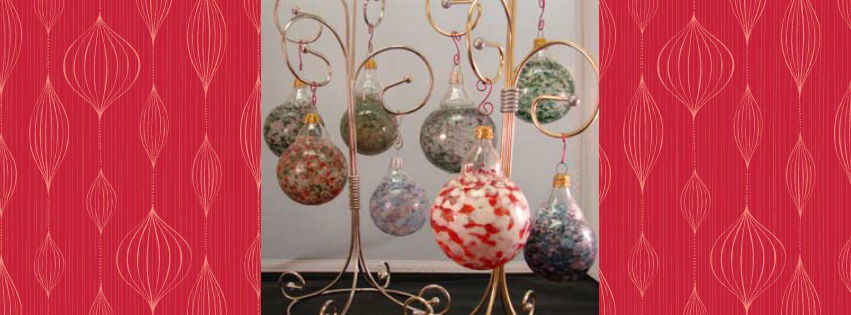Glass ornaments with colorful speckled patterns hang from golden, curly metal stands. The background is framed with red wallpaper featuring a repeating abstract pattern.