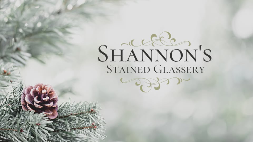 A frosty pine branch with a purple pinecone in the foreground; in the background, the text "Shannon's Stained Glassery" appears with decorative accents.