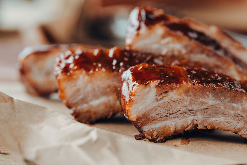 Four pieces of barbecued pork ribs with a glossy, caramelized glaze rest on brown parchment paper—perfectly tender and juicy, with a crispy outer layer—ideal for sharing during a Wisconsin Family Vacation feast.
