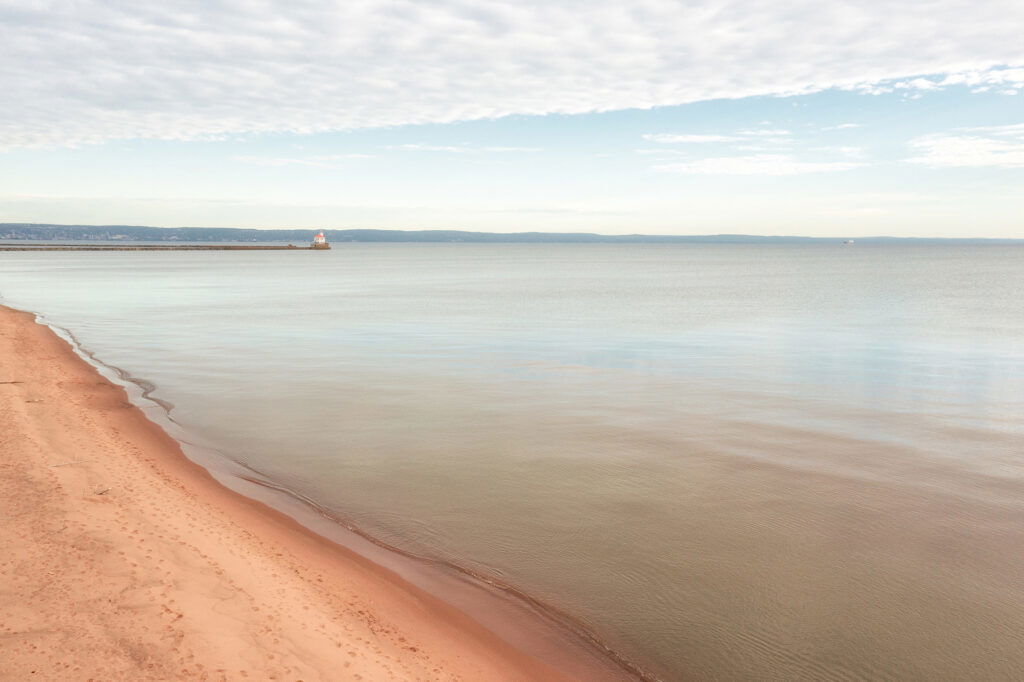 A sandy beach with a body of water and a pier, perfect for a relaxing Wisconsin Family Vacation.