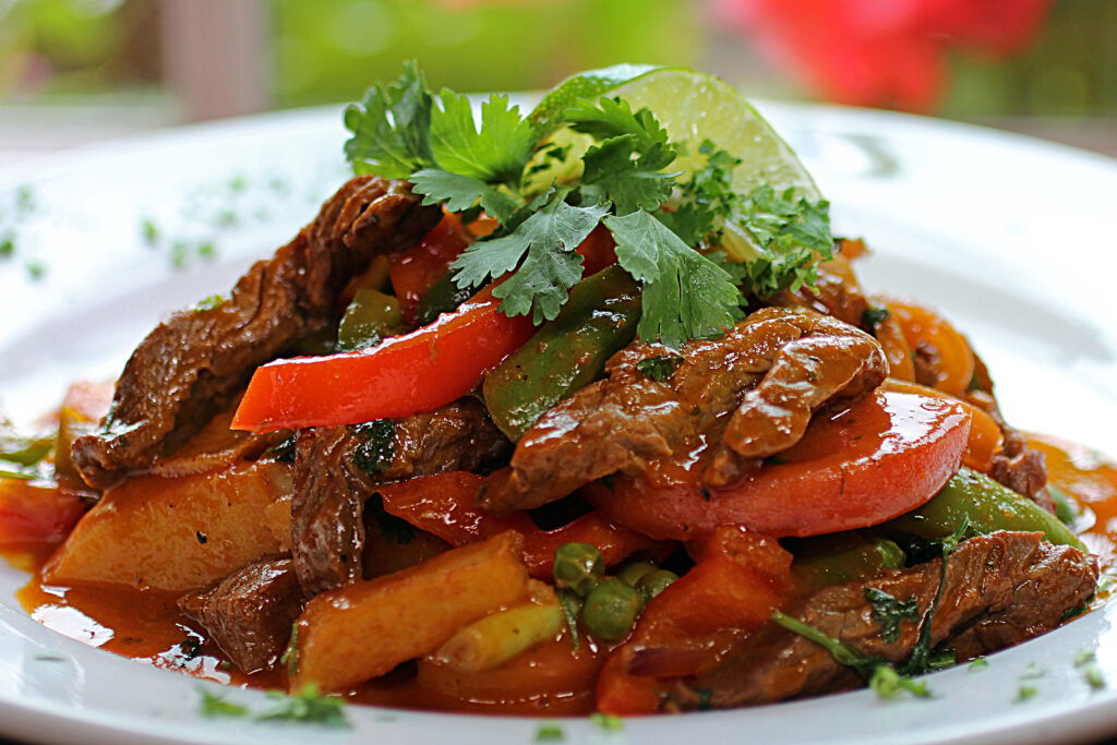A close-up of a colorful beef stir-fry with strips of beef, red bell peppers, green beans, peas, and potatoes, garnished with fresh cilantro and a lime wedge—just like dishes at top places to eat in Superior WI—served on a white plate.