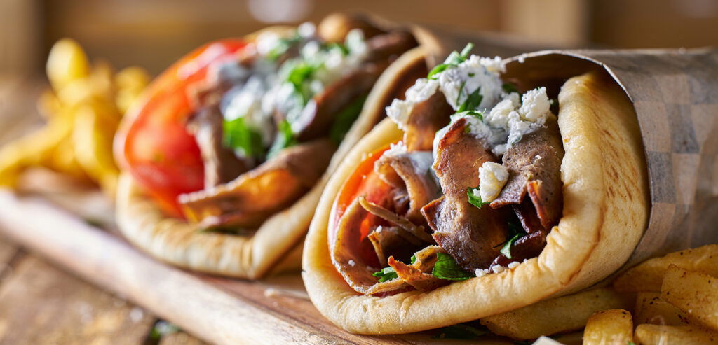 Two gyros wrapped in pita bread, filled with sliced meat, tomatoes, onions, parsley, and crumbled cheese, with a side of French fries—perfect for sharing on your Wisconsin Family Vacation.
