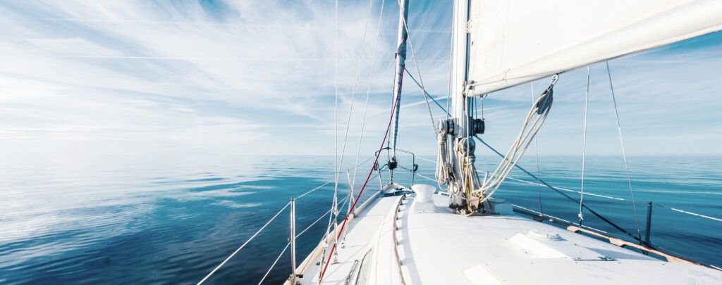 View from a sailboat’s deck looking out over calm, clear blue water under a bright sky with wispy clouds—perfect for weekend getaways in Wisconsin. The boat’s mast, rigging, and part of the sail are visible in the foreground.